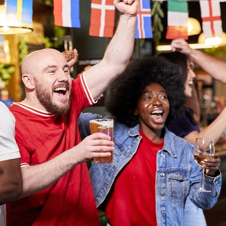 A mixed group of people holding a drink and cheering.