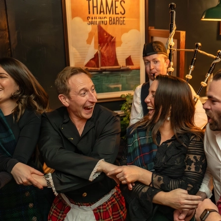 An image of a Bagpipe Player performing as people join hands to celebrate Auld Lang Syne within the interior function room during a Burns Night Event at The Crabtree.