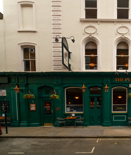 The exterior facade, signage, and seating area at The Plough in Bloomsbury, with flower baskets hanging from the walls.