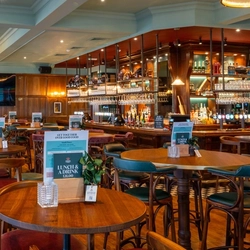 The bar and interior restaurant seating area of the Blue Posts in St James's, with a TV on the wood panelled wall, and glasses hanging in racks above the bar.