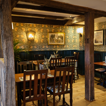 The wood panelled interior restaurant seating area with wooden tables and chairs, wooden beams, and framed artwork on the walls, at the Smiths Arms pub in Beckwithshaw.