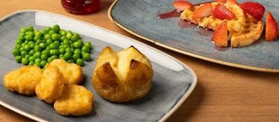 A plated children's meal with dessert and a drink is on a wooden table.
