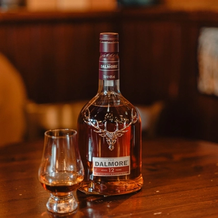 A bottle of The Dalmore Whisky on a table next to a whisky glass.