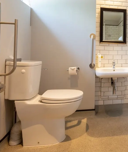 The interior accessible hotel bathroom with toilet and sink at the Cedars Inn.