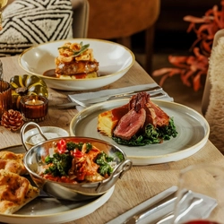 An advertising image of 3 Game Night Main dishes and a glass of red wine within the interior restaurant and seating area at The Foundry Bell.