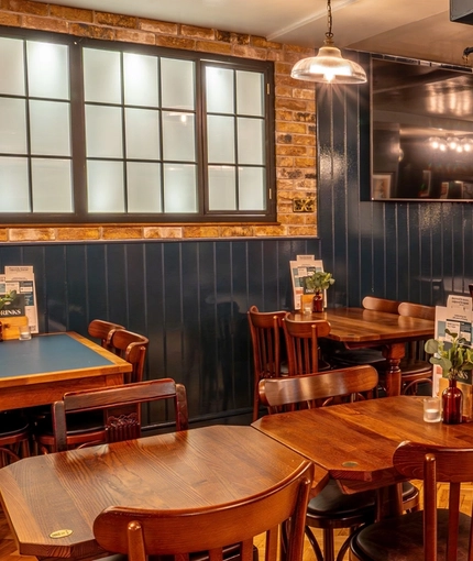 The interior restaurant seating area at the Monument in Whitechapel, with parquet floor and a TV on the wall.