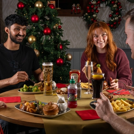 A group of people seated around a festive decorated table with plated meals in front of them.