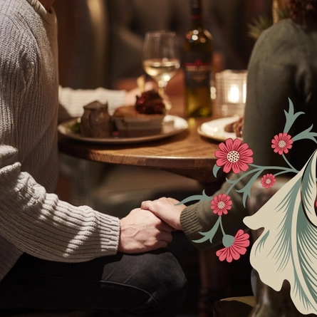 Two people sat at a table holding hands lower than the table. Low lighting, you can't see the peoples faces.