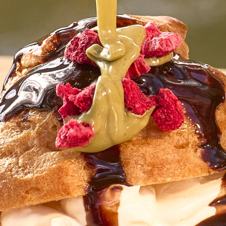 A banner showing a close up image of sauce being poured over a Pistatio Choux Bun available at Chef & Brewer venues.