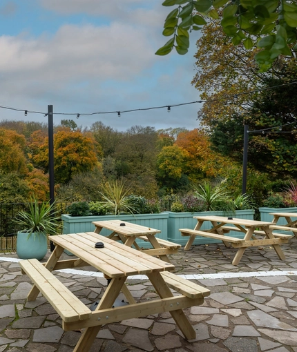 The exterior beer garden seating area at The White Lion in Frenchay, with wooden picnic tables, string lights overhead, and a view of the trees behind the pub.
