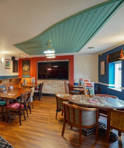 Interior dining area of a pub with a TV and a dartboard.