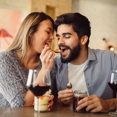 A couple sitting at a table feeding each other dessert.