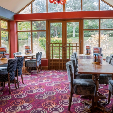 The interior restaurant seating area in the conservatory of The Royal Horse in Warwick, with wooden tables and upholstered seats.