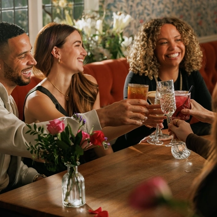 An image focusing on 3 customers sat with friends enjoying Valentines Day Drinks celebrating with a cheers sat at a table within the interior seating area of The Crown.