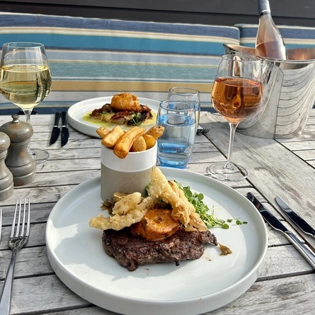 A plated steak with beef dripping chips and a plated chicken kiev with wine and water sat on an exterior table at The White Horses.