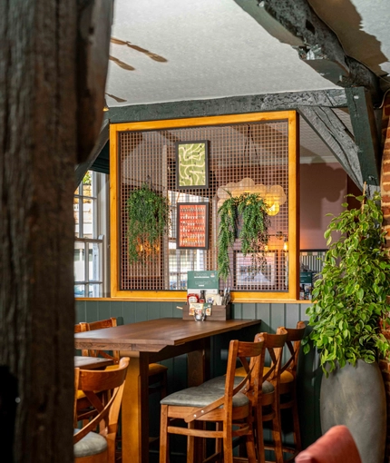 An interior restaurant seating area at The White Hart, with wooden beams, and potted plants hanging on the wall.