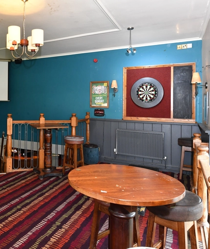 Interior dining area of a pub with a dartboard and a pull down projector screen.