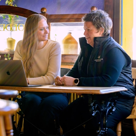 Two Women sat at a table with a laptop.