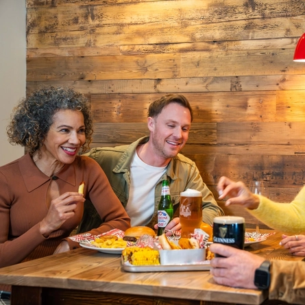An image showing a group of people sat around a table enjoying mains and sharer dishes with various drinks at a Flaming Grill venue.