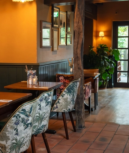 An interior restaurant seating area at The Malthouse Farm in Whittle-Le-Woods, with wooden beams, upholstered chairs and booth seat, and framed artwork on the walls.