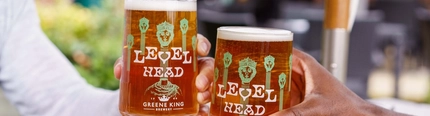 A close up image focusing on 2 pints of Level Head being held within an exterior beer garden seating area.