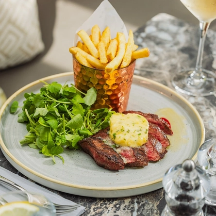 A plated steak and chips dish sat on a table within the exterior beer garden seating area at a Crafted venue.