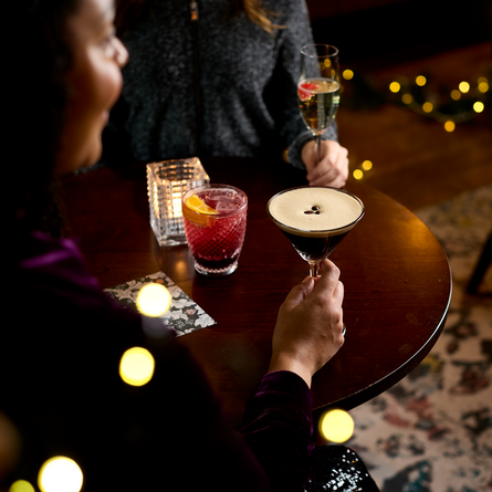 An image of 2 drinks being held and one sat on a table within the interior restaurant and seating area at a Chef & Brewer venue.