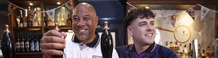 John Barnes and Mark Thorburn standing behind the bar at The Endbutt in Liverpool. John is holding one of the beer taps, and Mark is holding out a pint of beer.