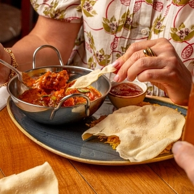 A hand dipping a poppadom into a balti dish of curry.