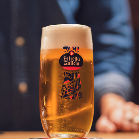 An image focusing on a pint of Estrella Galicia on an interior wooden table.