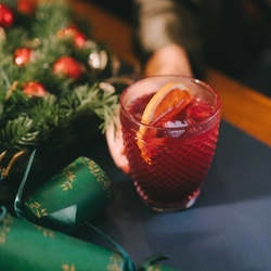 A hand resting on a festive decorated table is holding a cocktail type drink in a lowball glass.