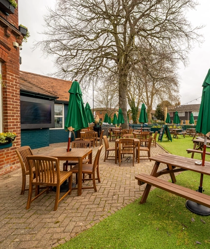 The exterior beer garden seating area of the Malvern Tavern, with wooden picnic tables, shade umbrellas, and string lights.