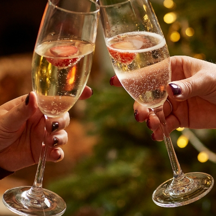 A product image of 2 glasses of white sparkling wine celebrating with a cheers within the interior of a Chef & Brewer venue.