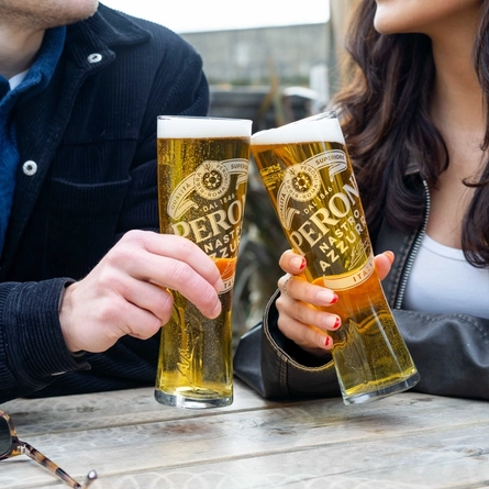 Two people sitting at a table in a beer garden, holding glasses of Peroni beer.