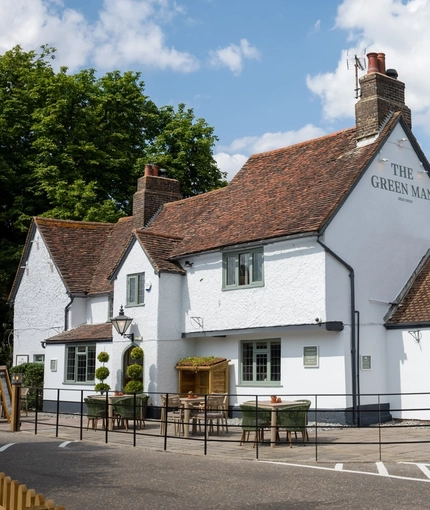 The exterior facade, signage, seating area, and car park of The Green Man in Great Offley, with accessible parking spaces near the entrance.