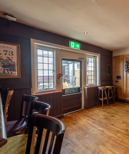 The interior games area at The Walkford in Walkford, with two dartboards on a wood panelled wall, and bar stool seating.