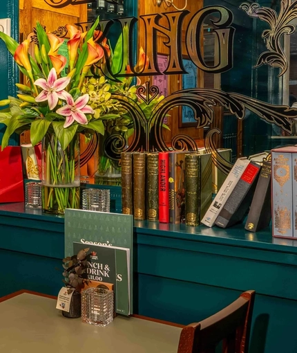 The interior restaurant seating area with a selection of decor including books, framed art prints and ornate painted mirror displaying the Greene King logo at The Lucas Arms.