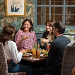 A group of people sitting around a table smiling and having a meal, with drinks in their hands.