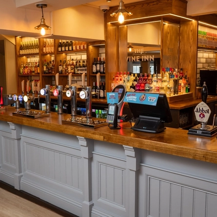 A close up view of the bar at The Vine Inn in Ower, with bottles of wine and alcoholic spirits on wooden shelves behind the counter.