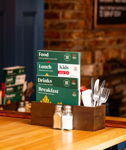 A close up view of salt, pepper, and a wooden box containing menus, cutlery, serviettes, and a bottle of tomato sauce, on a wooden restaurant table inside The Windmill Inn.