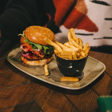 A festive decorated wooden table holding a plated burger and fries.  There is the torso of a woman holding a glass of sparkling wine sat at the table.