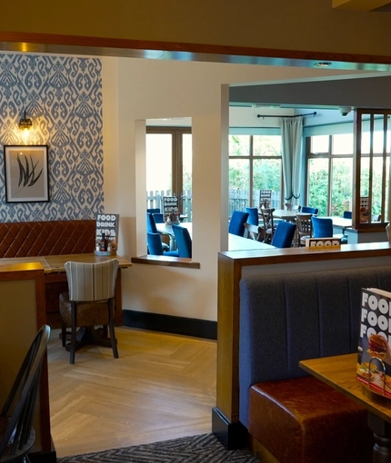 An interior restaurant seating area at The Steam Turbine in Rugby, with upholstered booth seating, and framed artwork on the walls.