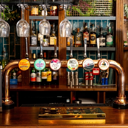 A close up view of a golden drinks tray and the beer taps for Hazy Day, Level Head, Old Mout Berries & Cherries, Inch's, San Miguel, and Birra Moretti; on the bar at The Talbot in Worcester.