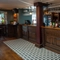 The wood panelled bar at The Ship; with a patterned tile floor in front of the bar, golden drinks trays on the counter, and glasses hanging in racks overhead.