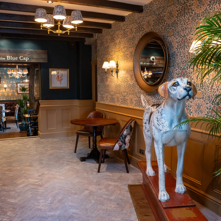 The interior of The Blue Cap in Sandiway, with patterned brick floor, wooden beams on the ceiling, and a large statue of a dog.