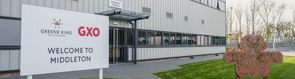 The exterior facade of the Greene King supply chain depot with a welcome sign reading 'Greene King Bury St Edmunds GXO, welcome to Middleton.'