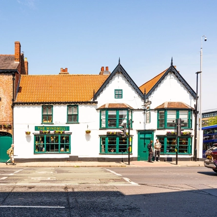 A view from across the road of the exterior facade and signage of The Windmill Inn in York, with flower baskets hanging on the wall.