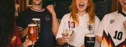 An image showing a group of friends stood at a table watching a football match and enjoying a selection of drinks within the interior seating area at a Greene King venue.