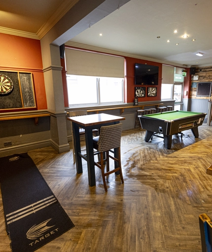Interior dining area of a pub with a pool table, a TV and a dartboard.