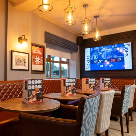 An interior restaurant seating area at The Gatehouse, with upholstered chairs and booth seats, and a TV on the wall.